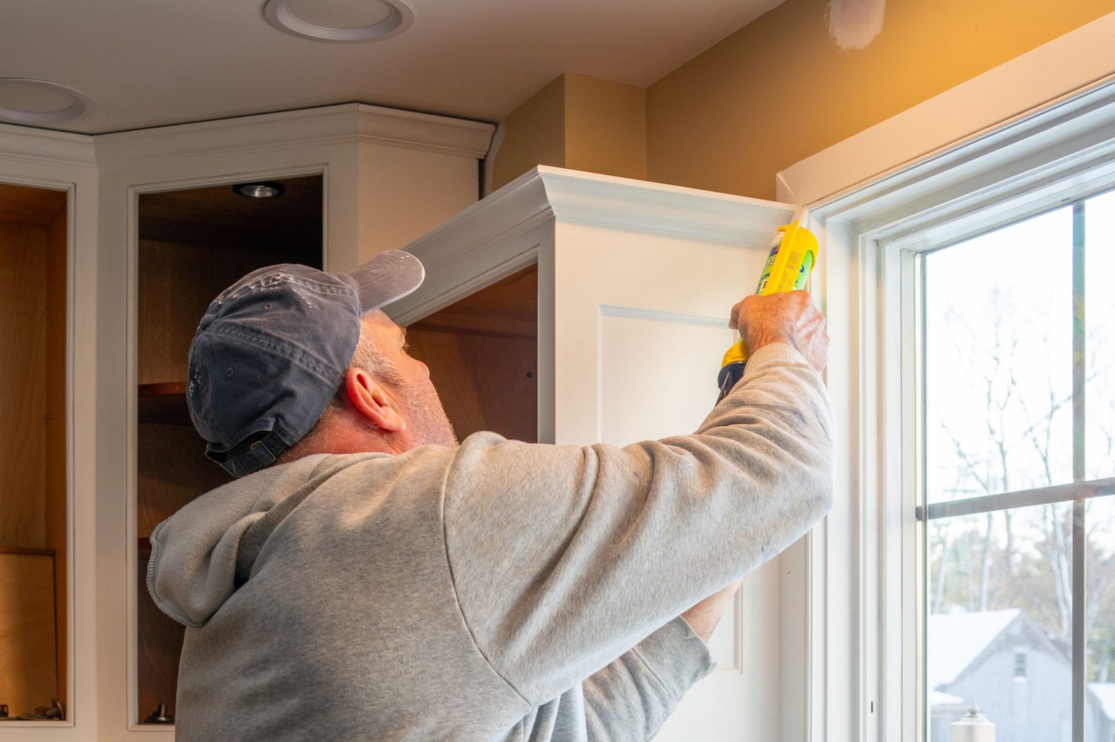 Installer caulking an upper cabinet during installation